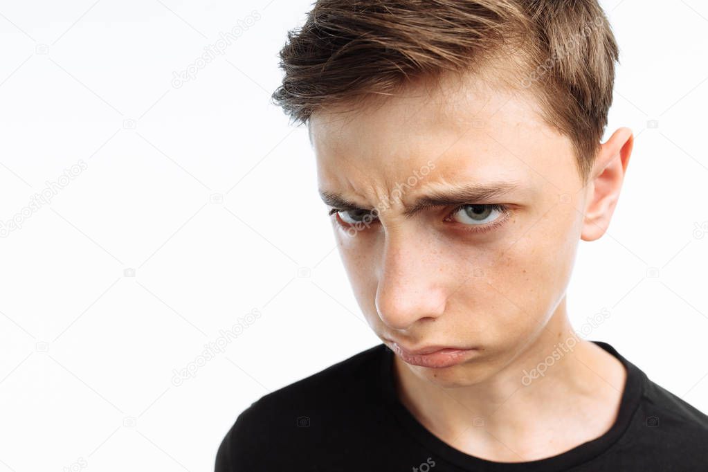 Portrait of a teenager, a guy showing emotions of sadness and resentment, in a black t-shirt, on a white background,