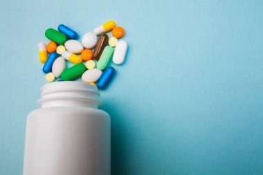 Çok renkli tablet ve kapsül kalp şeklinde, tablet, ilaç tıp hapları üzerinde mavi arka plan, analjezik hastalıklara karşı beyaz şişe