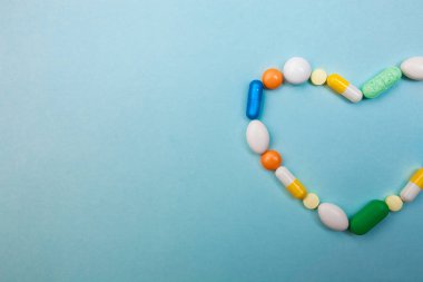 Çok renkli tablet ve kapsül kalp şeklinde, tablet, ilaç tıp hapları üzerinde mavi arka plan, analjezik hastalıklara karşı beyaz şişe