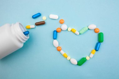 Çok renkli tablet ve kapsül kalp şeklinde, tablet, ilaç tıp hapları üzerinde mavi arka plan, analjezik hastalıklara karşı beyaz şişe