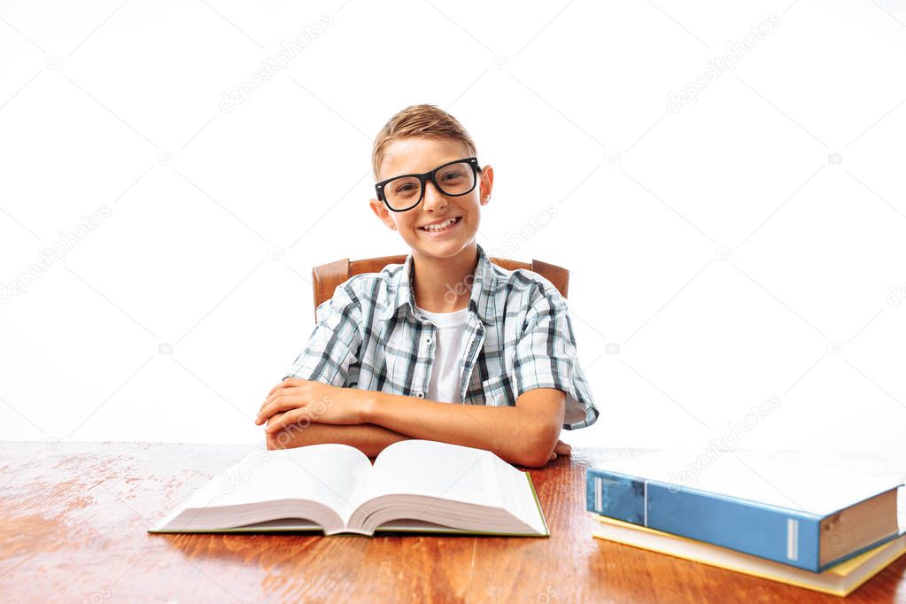 Young handsome teen guy reading book sitting at table, schoolboy or student doing homework, in Studio on white background