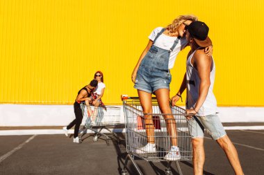 Bir grup genç insan arabaları üzerinde sürmek büyük bir eğlence, sepeti, süpermarket, yanında oturan arabaları üzerinde oturan aşıklar öpüşmek, aşık çiftler güneşli havalarda eğlenmek