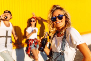 bir grup arkadaşıyla arka plan üzerinde güzel bir kızın portresi, bir içki ile cam şişe ile gençlerin grup çekilin süpermarket, sarı bir arka plan üzerinde yakın arkadaş gel dolu, neşeli ruh halinde güneşli bir gün