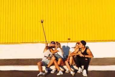 Bir grup arkadaşıyla kaldırımda, Genç insanların bir selfie sopa, neşeli Şirket, güneşli gün ile fotoğraf çekmek şirket oturan bir selfie yapar