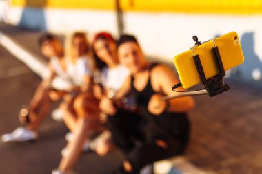 Bir grup arkadaşıyla kaldırımda, Genç insanların bir selfie sopa, neşeli Şirket, güneşli gün ile fotoğraf çekmek şirket oturan bir selfie yapar