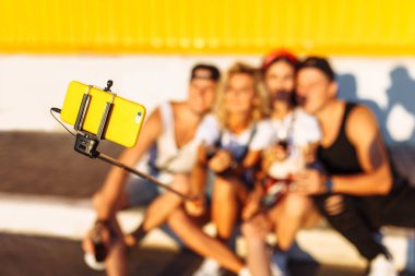 Bir grup arkadaşıyla kaldırımda, Genç insanların bir selfie sopa, neşeli Şirket, güneşli gün ile fotoğraf çekmek şirket oturan bir selfie yapar
