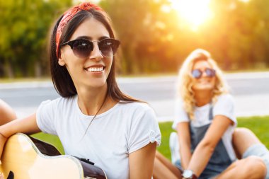 Gün batımı çimlere yakın çekim güzel gülümseyen kız bir grup arkadaşıyla gitar, iyi yaz ruh oynarken arka plan üzerine oturan, eğleniyor arkadaş şirket