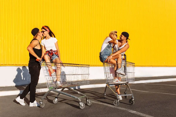 亲吻恋人坐在推车上 在超级市场附近 一个伟大的消遣 一群年轻人乘坐推车 情侣在阳光明媚的天气里玩得开心 — 图库照片