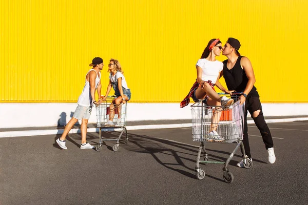 朋友们骑在推车上 在超市附近 一个伟大的消遣 一群年轻人骑在推车上 相爱的情侣在阳光明媚的天气里玩得开心 — 图库照片