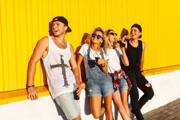 a group of young people with glass bottles with a drink stand near the supermarket, on a yellow background, friends come off in full, cheerful mood, Sunny day, Lifestyl concept, catch moments together with best friends