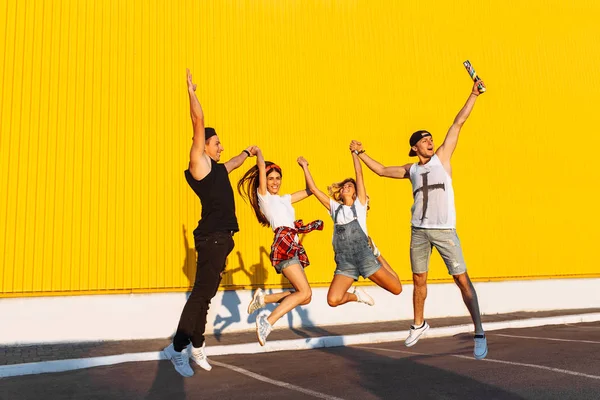 黄色の背景は 若い人たちを祝っていて楽しい 夏気分で街に歩いている友人のグループに紙吹雪と美しいクールな若いジャンプを配置 駐車場でのパーティー — ストック写真