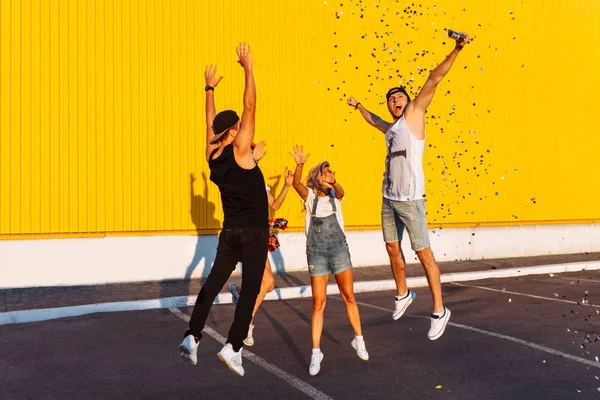 黄色の背景は 若い人たちを祝っていて楽しい 夏気分で街に歩いている友人のグループに紙吹雪と美しいクールな若いジャンプを配置 駐車場でのパーティー — ストック写真