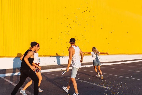 美丽凉爽的年轻跳跃与五彩纸屑在一个黄色的背景 一群年轻人庆祝和有乐趣 夏天的心情 朋友们走在城市的地方 党在停车场 — 图库照片