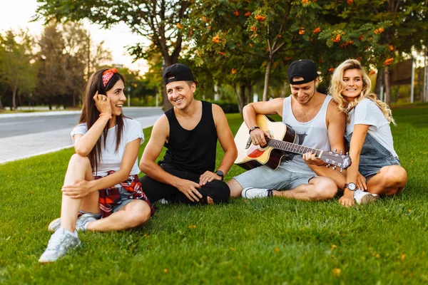 公司的朋友在日落时玩得开心 坐在草地上 弹吉他 好夏天的心情 — 图库照片