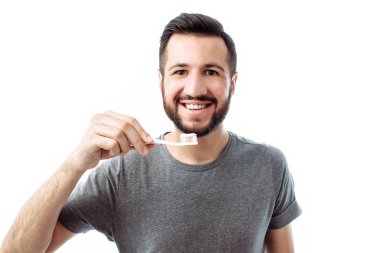 Gri t-shirt izole bir beyaz arka plan üzerine bir diş fırçası ile sakallı bir gülümseyen genç adam hipster portresi.