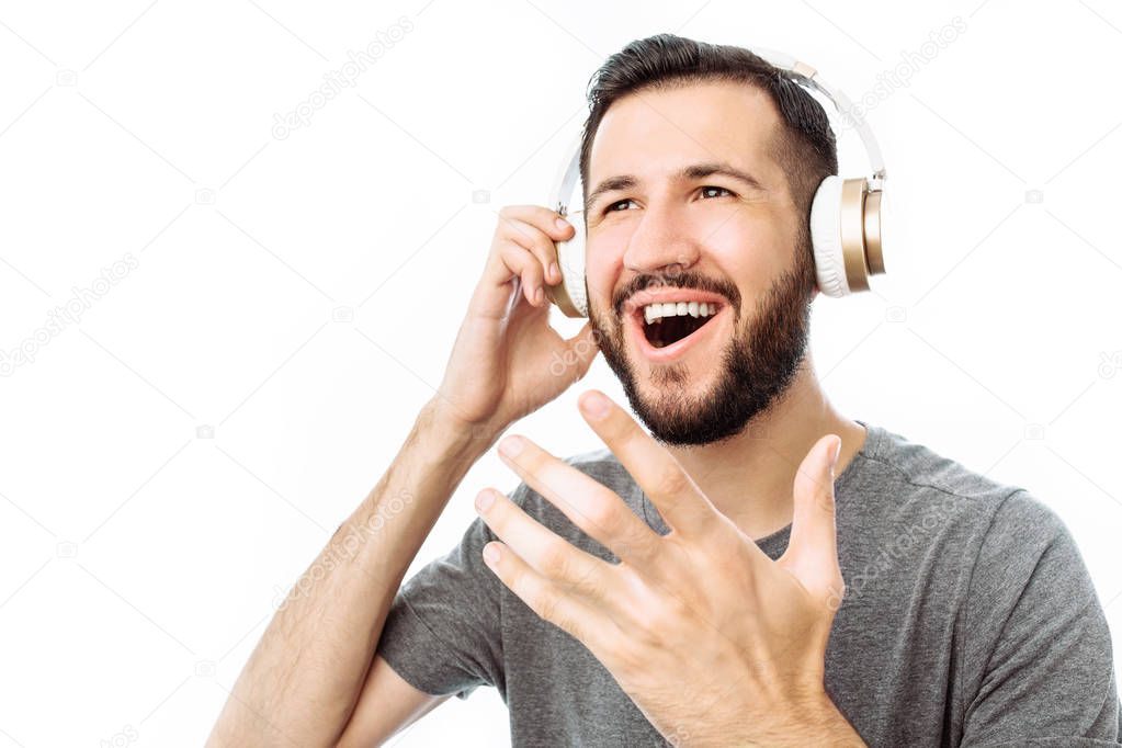 Young attractive bearded man sings loudly, and listens to music in headphones while standing isolated on white background,