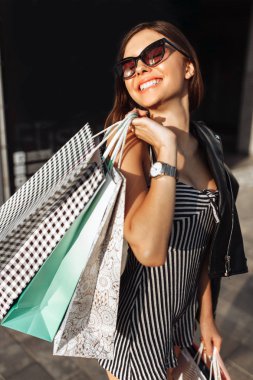 Bir genç gülümseyen kız başarılı bir alışveriş torbaları ile sokakta yürürken elinde sahiptir
