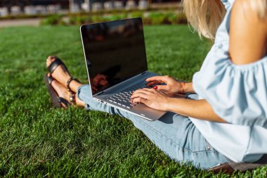 Mutlu yakışıklı öğrenci, parkta otururken çimenlikte dizüstü bilgisayarda çalışan genç kadın