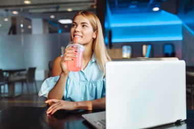 Şık genç bir öğrenci, süre işten dinlenme, bir dizüstü bilgisayar ile oturup ve birisi ile bir toplantı için bekleyen bir kokteyl ve gülümsüyor, içecekler