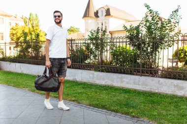Şık hipster şehirde yürüyüş onun elinde bir çanta ile beyaz bir t-shirt, güneş gözlüğü, içinde sakallı