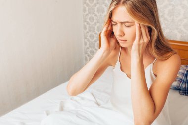 Pijama onu yatakta üzerinde oturan genç güzel kız oda ve ellerini kafasına şiddetli bir baş ağrısı duygu presler