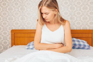 Sabah ve midesini tutan yatakta oturan bir genç kız uyandım, yüzünü ağrı gösterilen kız biniyor. Karın ağrısı, belirti, hayız, acı kavramı.