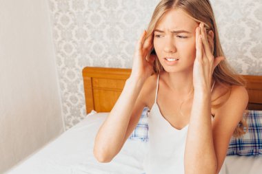 Pijama onu yatakta üzerinde oturan genç güzel kız oda ve ellerini kafasına şiddetli bir baş ağrısı duygu presler