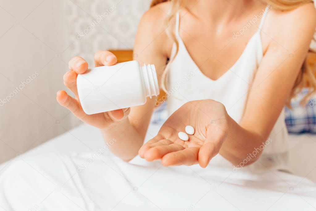 Woman hands taking pills from banks, sitting in bed and feels bad, close-up
