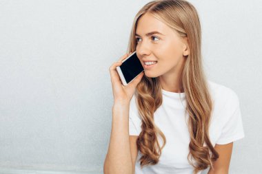 Gri bir arka plan telefonda konuşurken bir beyaz t-shirt giyen güzel genç kız