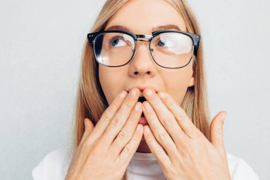 Duygusal bir genç sarışın ani haberlerde inanamıyorum geniş ağzını açar, sürpriz ifade eder, şeffaf gözlük takar, gri bir arka plan üzerinde duruyor.