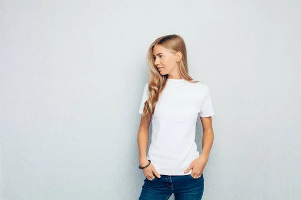 一个年轻漂亮的女孩身着白色 T恤站在灰色的墙壁背景姿势的形象 — 图库照片