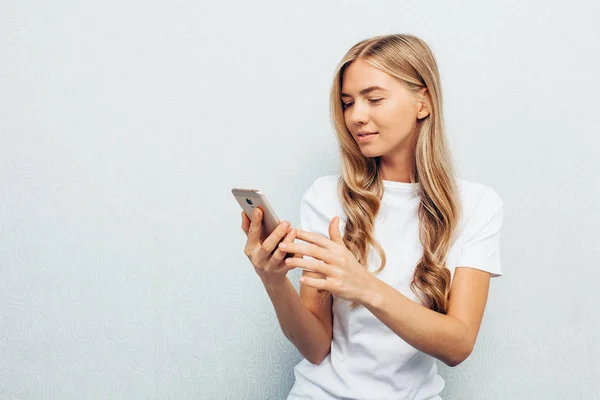 Genç güzel kız beyaz gömleği giyince telefon tutarak ve ekran yere cross-legged, oturma, bakarak giymiş izole üzerinde gri arka plan