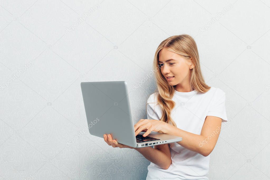 Portrait of happy woman wearing white t-shirt sitting on the floor with laptop on grey background