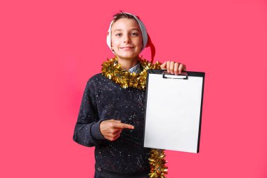 Noel Baba şapkası giyen genç adam ve onun boynuna gelin teli ile bir tablet ile temiz bir sayfayla tutarak ve ona, parmakla planlıyor önümüzdeki yeni yıl kırmızı bir arka plan üzerinde