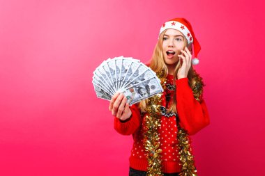 Kırmızı kazak ve Santa şapka şok bir kız telefonda konuşurken ve duygular sevinç kırmızı bir arka plan üzerinde tasvir para tutuyor. hakkında Noel, para, holding