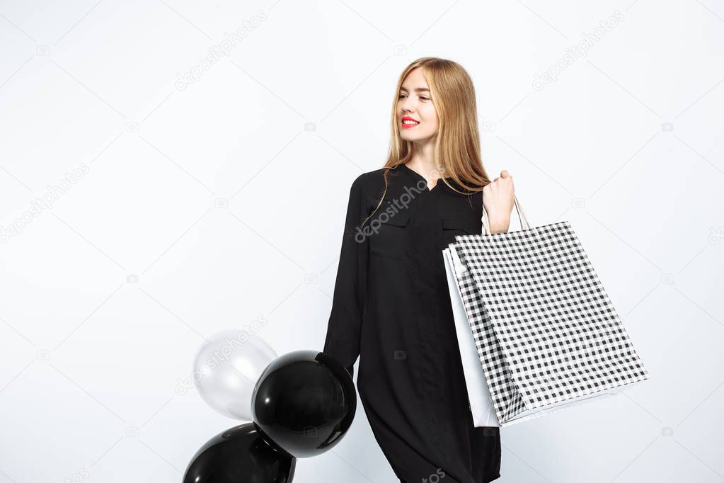 happy woman in black dress and with red lips holding bags and black balls, happy girls after shopping, Black Friday on white background