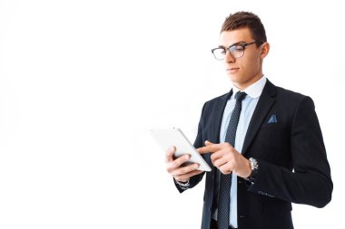 Bir takım elbise ve gözlük, kendine güvenen genç yakışıklı adam beyaz bir arka plan üzerinde duran bir dijital tablet üzerinde çalışan