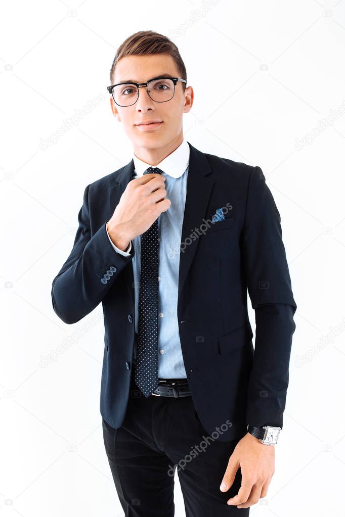 Successful businessman in glasses and suit, carefully straightens tie and posing on isolated white background