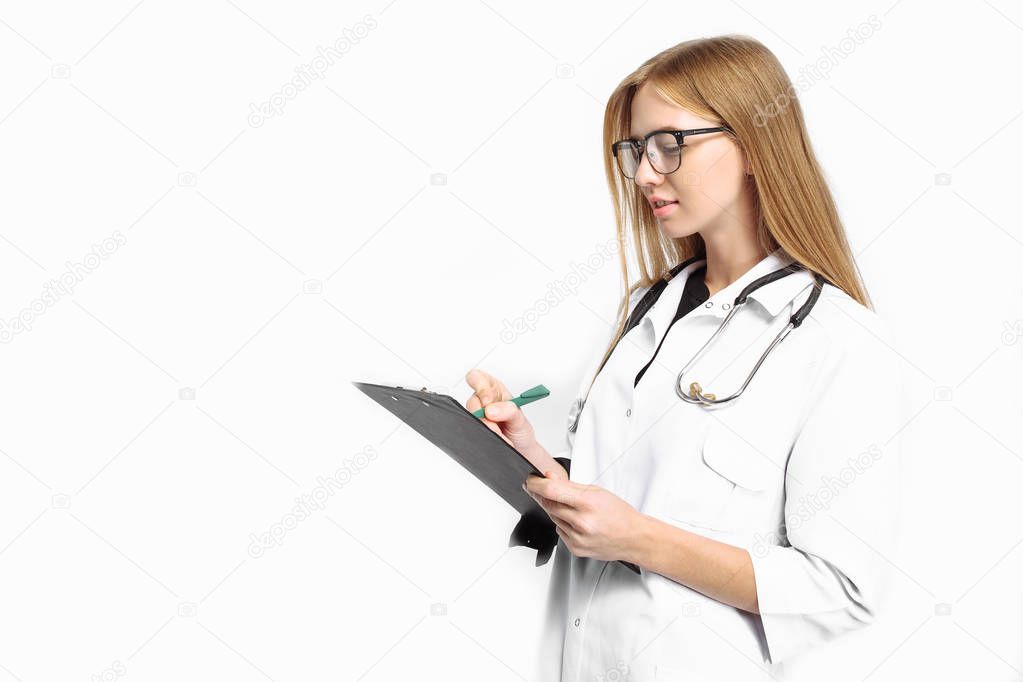 A trainee girl, with glasses, with a stethoscope around her neck, writes the diagnosis in her folder on a white background. medicine concept