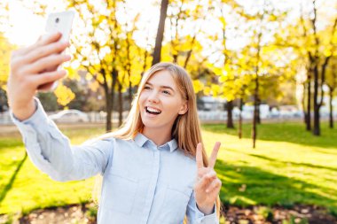 Mutlu genç kız parkta bir fotoğrafını alarak bir telefon ile