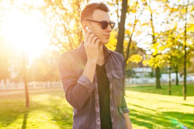 Genç adam şık giysiler içinde kablosuz kulaklık üzerinden müzik ve park açık havada yürüyüş giymiş