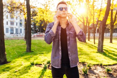 Genç adam şık giysiler içinde kablosuz kulaklık üzerinden müzik ve park açık havada yürüyüş giymiş
