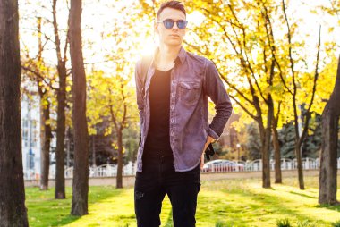 Şık giysiler içinde güneş gözlüğü, giyinmiş bir çanta ile genç bir öğrenci parkta yürüyor,