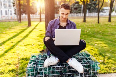 bir bankta oturan rahat giysiler içinde ile bir dizüstü bilgisayar, bir dizüstü bilgisayar ekranında, bir gün batımı karşı arıyorsunuz çalışan adam