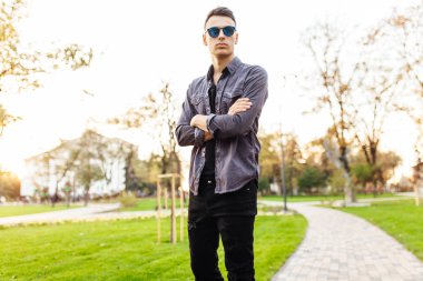 gün batımına karşı parkta çekici adam şık elbiseler, güneş gözlüğü, giyinmiş yürür
