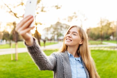 Bir akıllı telefon ile bir parkta duran mutlu bir kadın portresi. O kendini çekiyor
