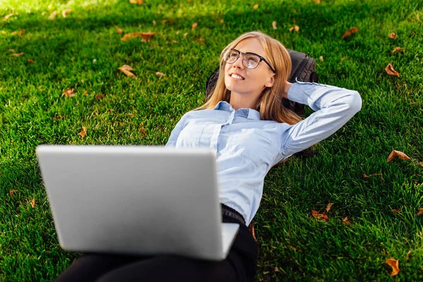 Przemyślane Dziewczyna Okularach Leżąc Trawie Parku Laptopem Marzy Czymś Uśmiechem — Zdjęcie stockowe