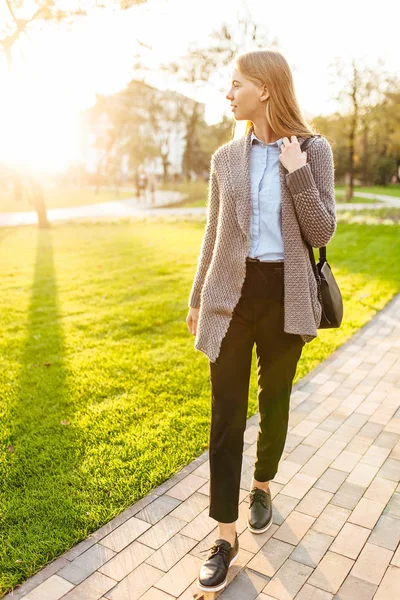 Jovem mulher bonita andando no parque, contra o pano de fundo de um belo pôr do sol — Fotografia de Stock