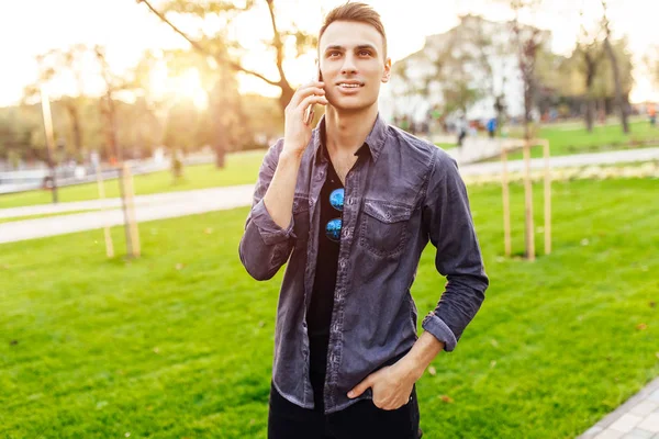 Handsome young man talking on the phone, walking in the park — Stock Photo, Image