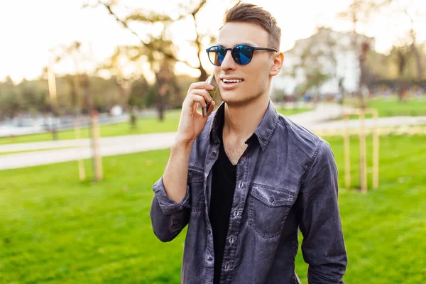 Χαρούμενος ο τύπος σε γυαλιά ηλίου, μιλώντας στο τηλέφωνο, περίπατο στο πάρκο — Φωτογραφία Αρχείου